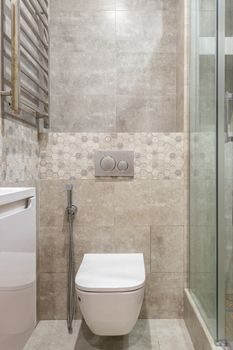 lave-mains d'angle compact au-dessus d'un WC suspendu blanc, dans un petit espace carrelé de gris clair, lumière naturelle douce
