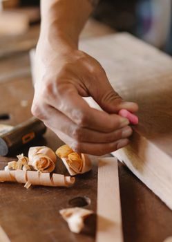 gros plan de mains insérant une languette de contreplaqué dans une rainure fraisée sur la tranche d'un plan de travail en bois clair, atelier avec copeaux visibles
